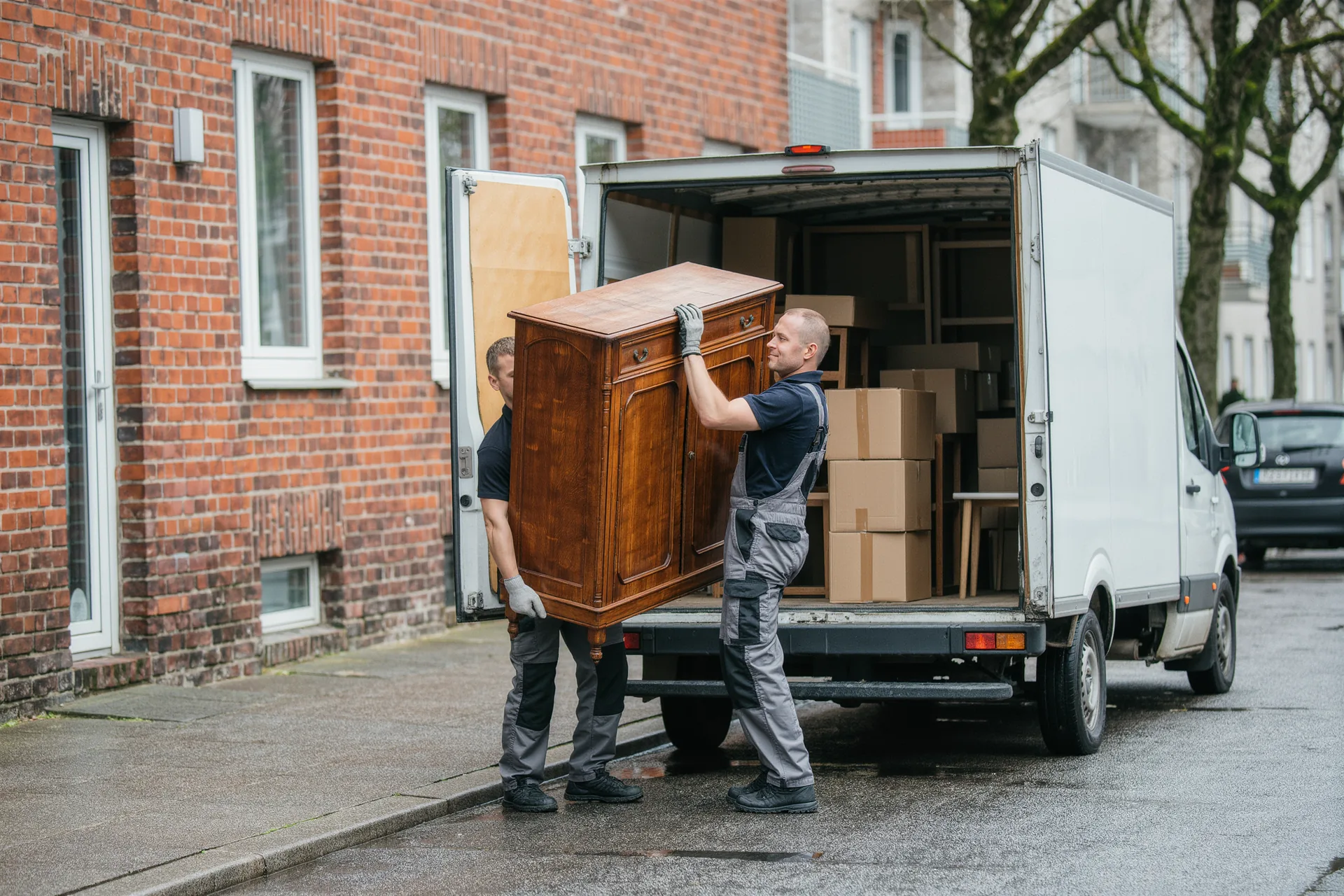 Zwei Mitarbeiter tragen einen alten Schrank zum Transporter