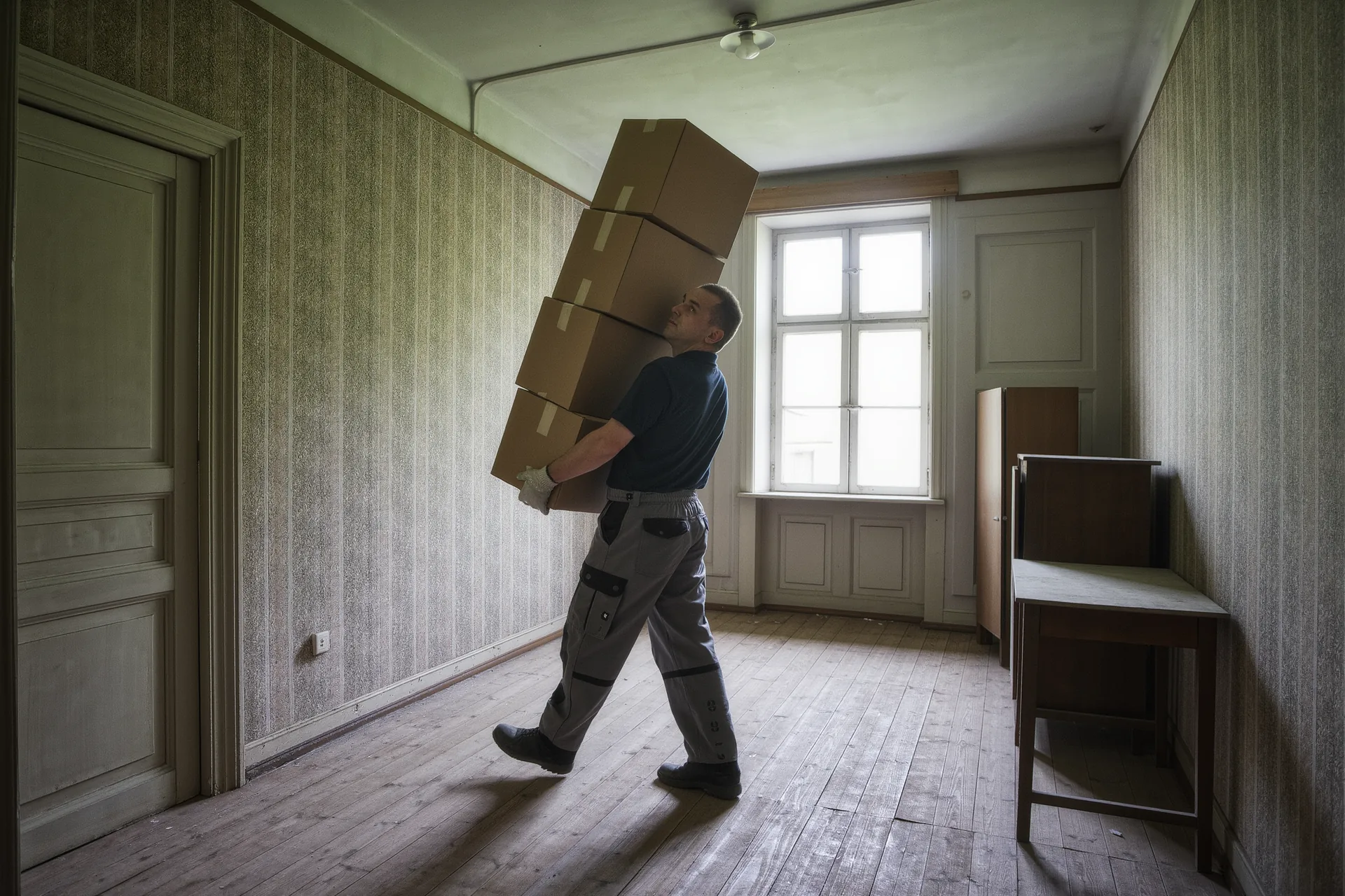 Mitarbeiter trägt einen Stapel Kartons durch ein leergeräumtes Altbauzimmer